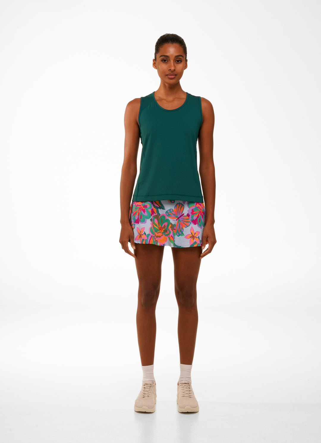 Woman wearing a green tank top and colorful floral skirt on a white background