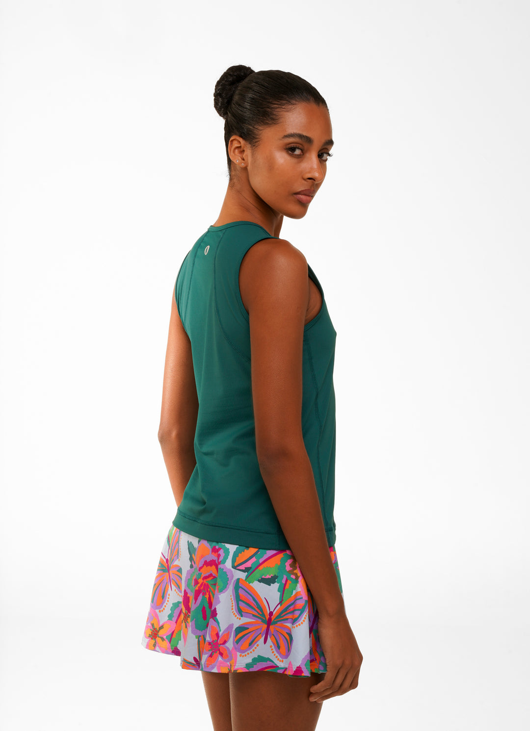 Woman wearing a green sleeveless top and colorful butterfly-patterned skirt on a white background