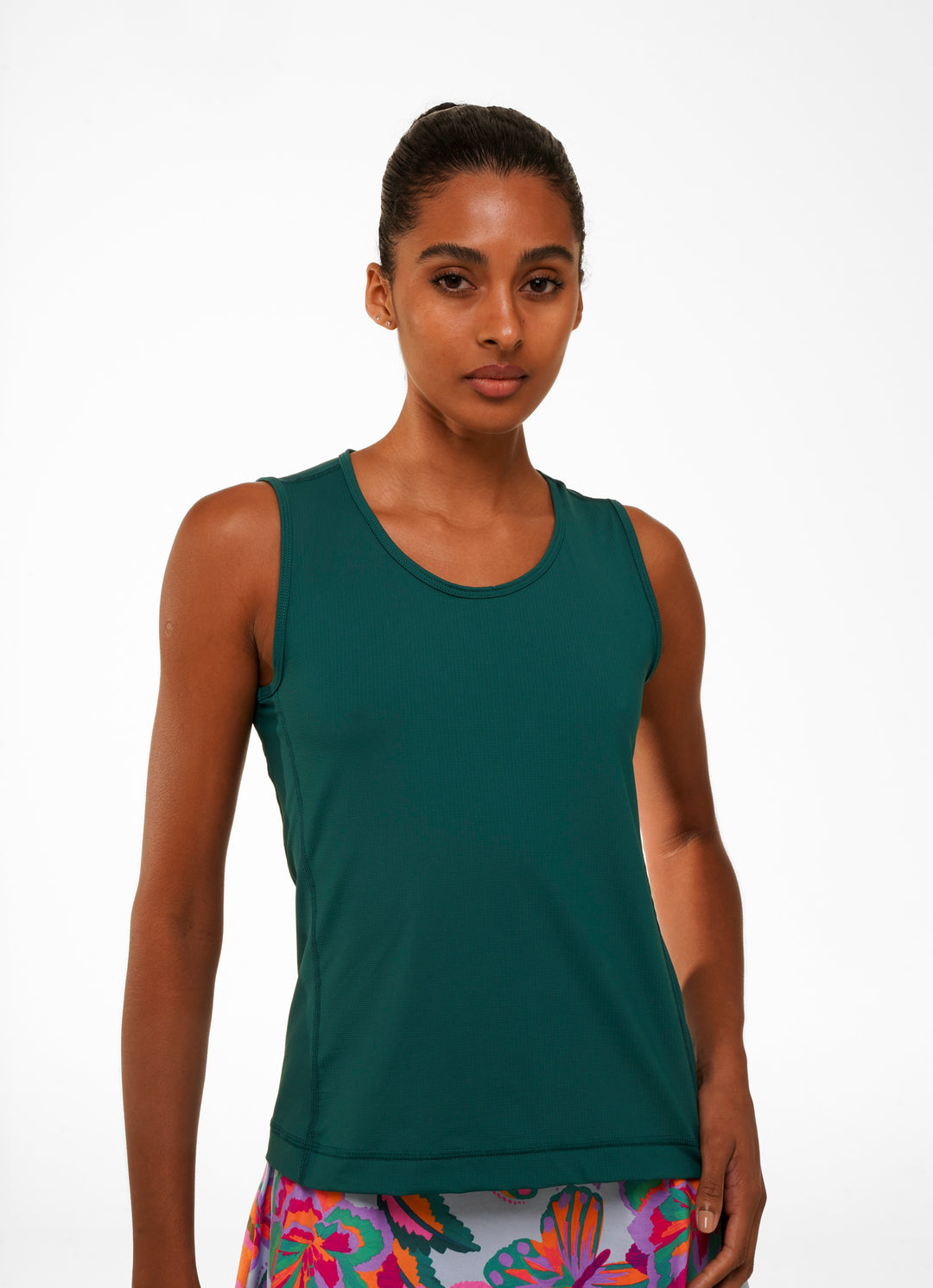 A female model wearing a green tank top with a round neckline and sleeveless design.