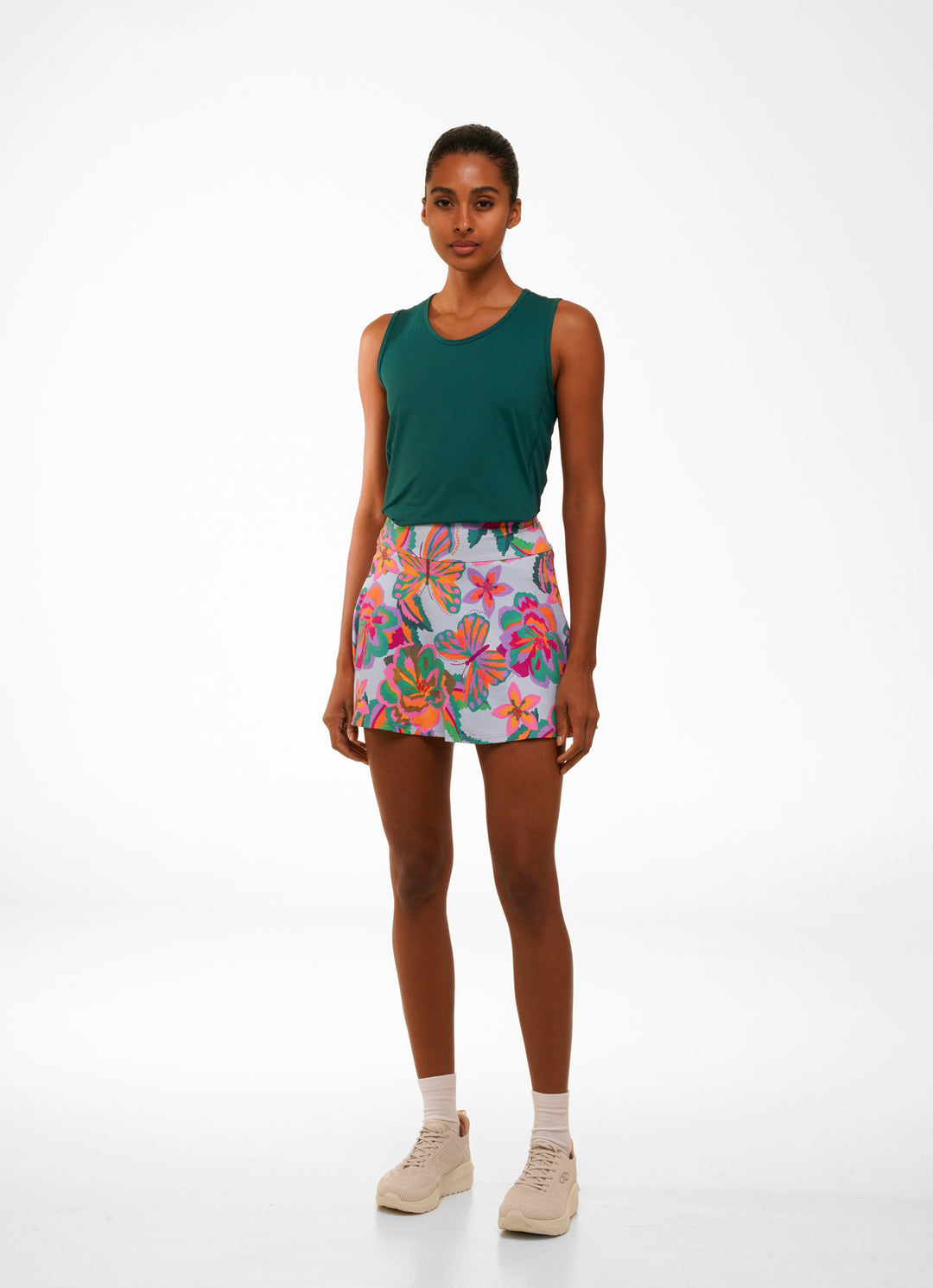 Woman wearing a green sleeveless top and colorful floral shorts on a white background