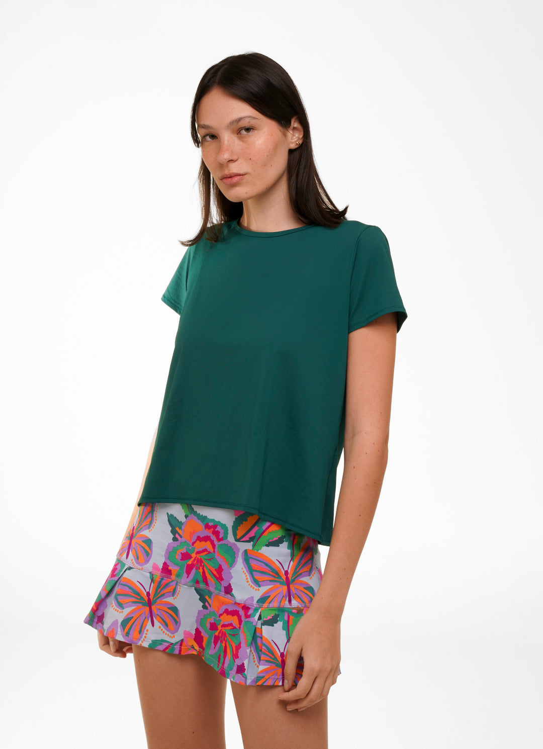 A woman wearing a green short-sleeve shirt paired with a multicolored skirt with a floral pattern.