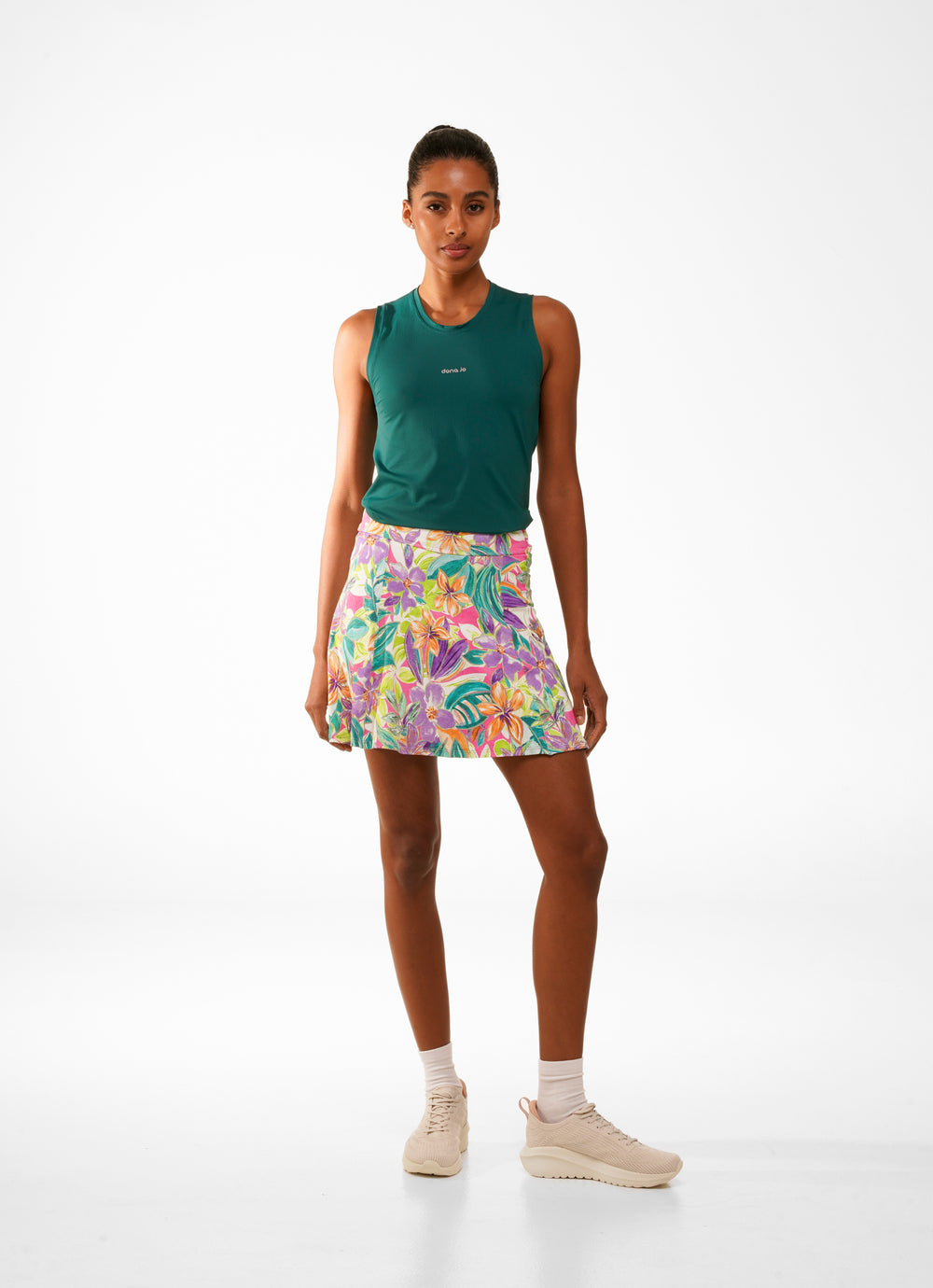 Woman in green sleeveless top and colorful floral skirt on a white background