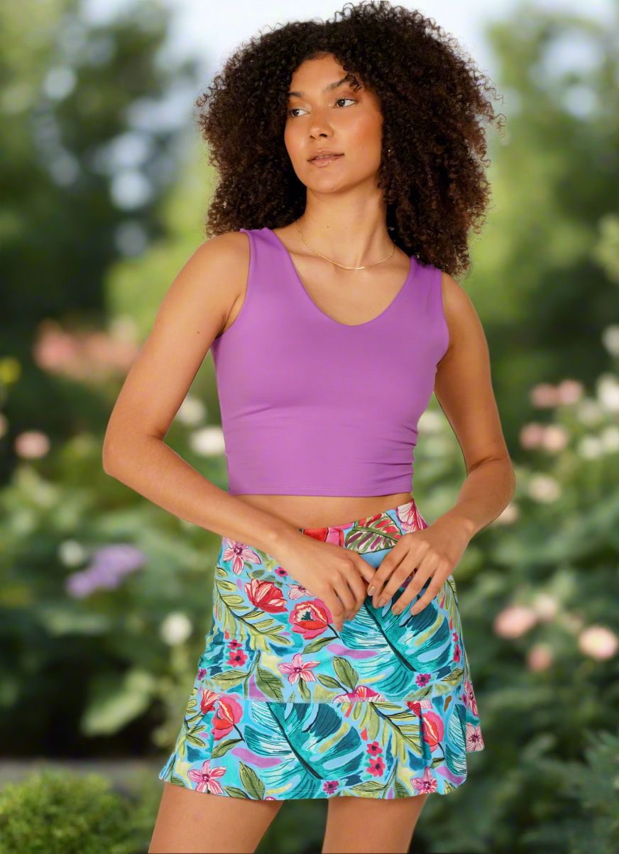 Woman wearing a purple tank top and colorful floral skirt on a plain background